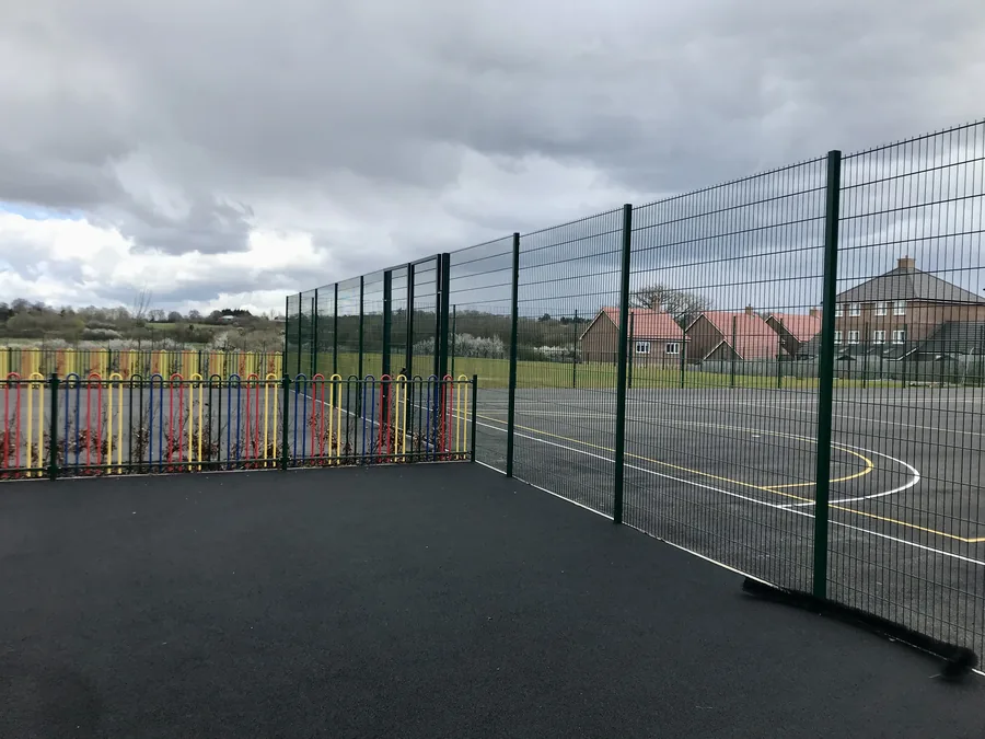Multi-coloured bow-top railings beside green weld mesh fencing at the new-build school