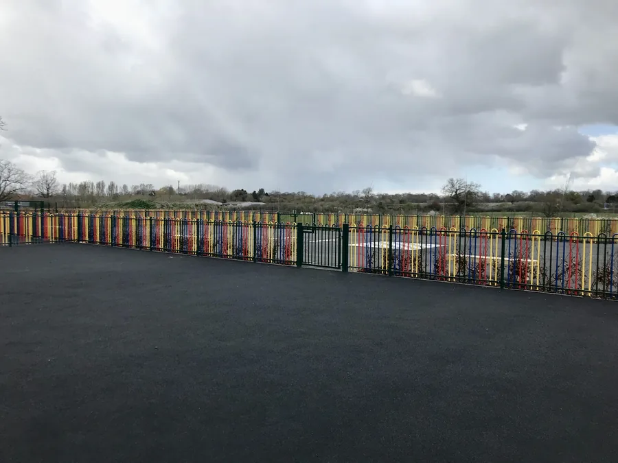 Colourful bow-top playground railings with the school sports enclosure behind