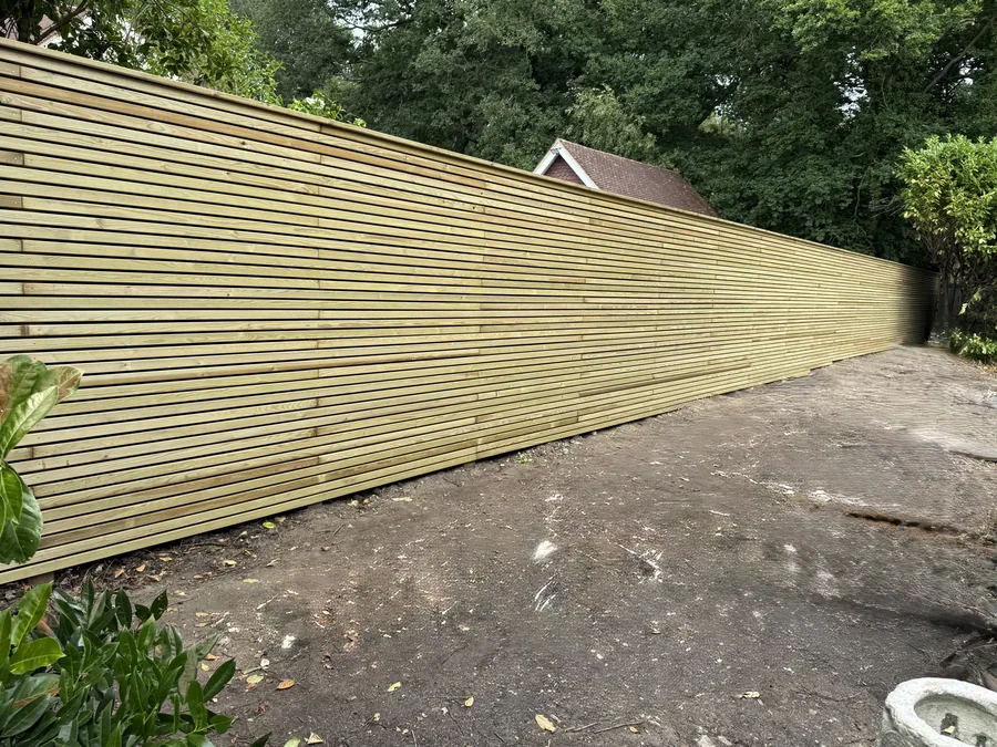 Finished green pressure-treated slatted boundary fence with a wide custom capping rail
