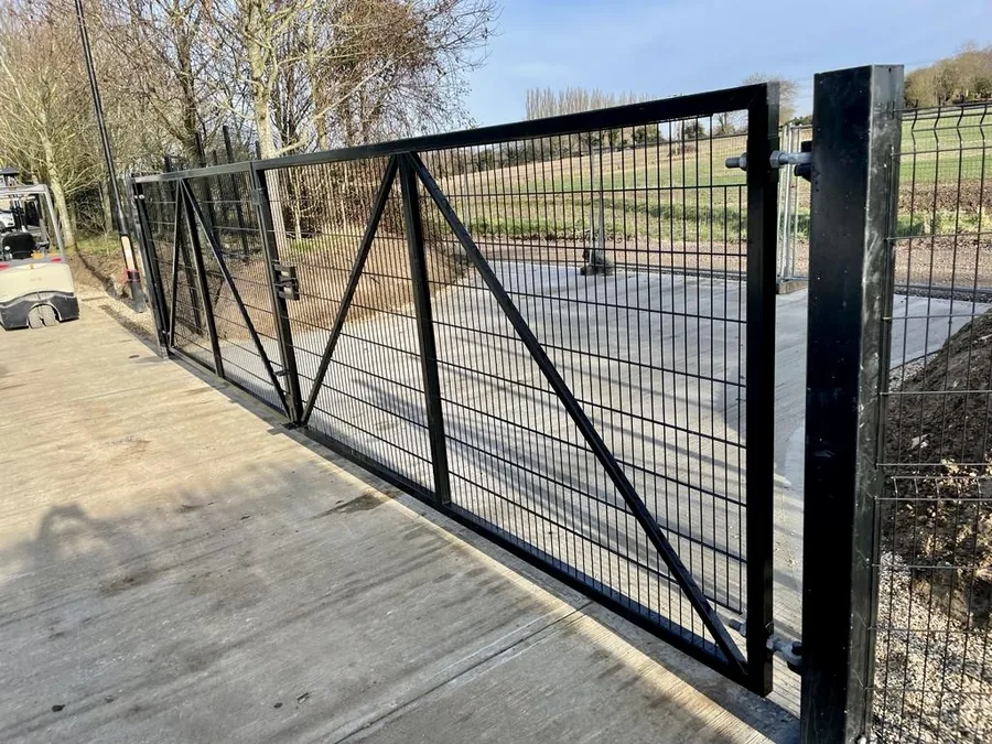 Black metal mesh driveway gates at a rural entrance