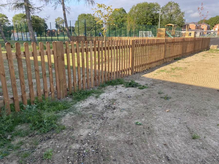 Timber fencing running alongside a green mesh school sports court