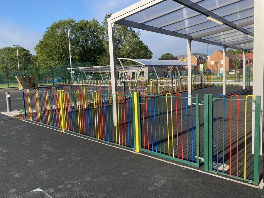 Completed multi-coloured bow-top school railings and green access gates in bright daylight
