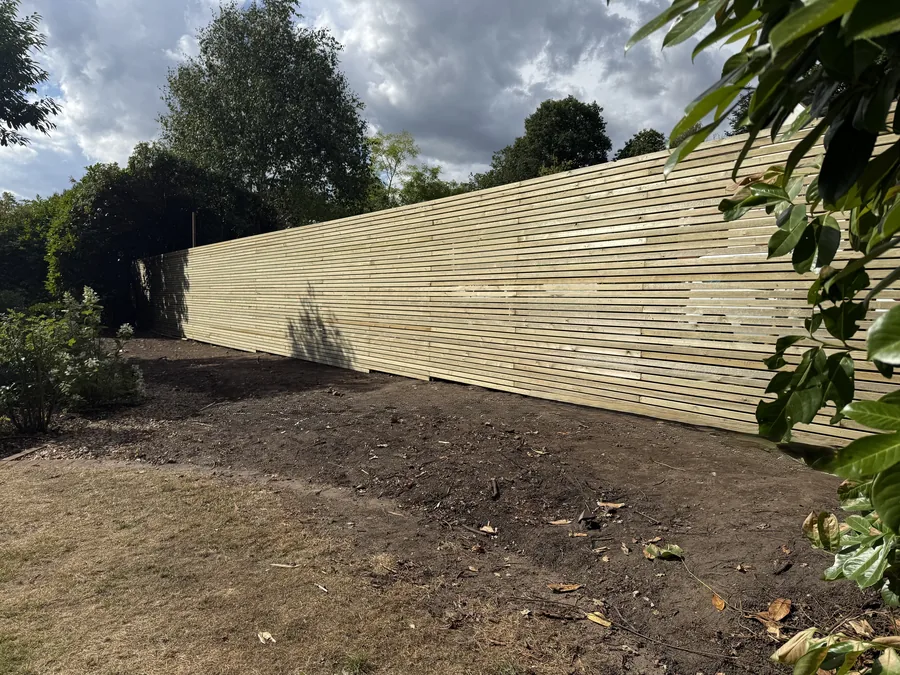Completed green pressure-treated timber slatted fence along the garden boundary