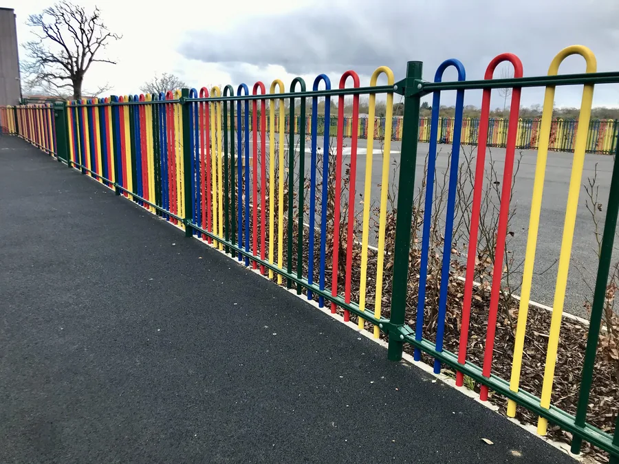 Green weld mesh sports fencing beside multi-coloured school railings