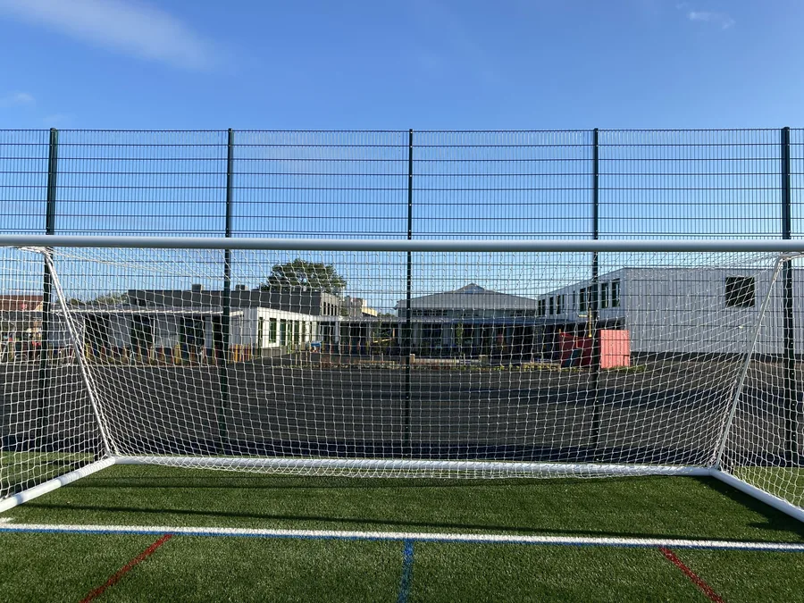 High green ball-stop mesh fencing behind a football goal on the 4G pitch